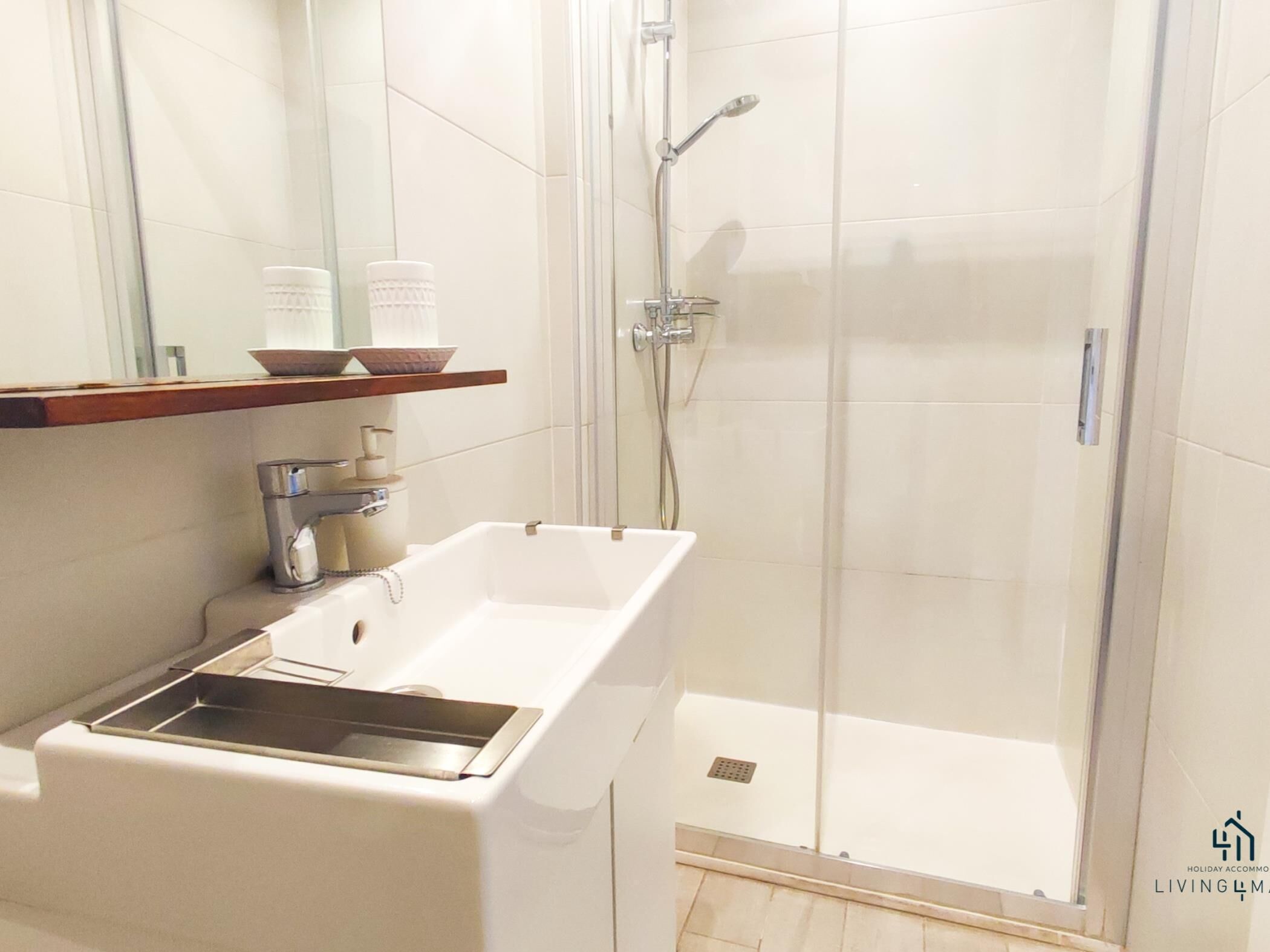 Un baño con lavamanos blanco, espejo, cabina de ducha e inodoro.