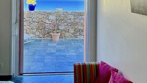 A room with a view of the sea through an arched doorway, a potted plant, and a colorful chair.