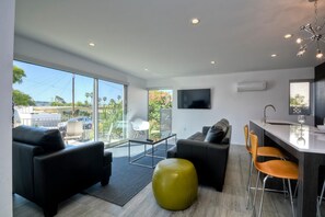 Relax in a spacious living area with a sofa, ottoman, and dining space, featuring a flat-screen TV and a large window with an outdoor view.