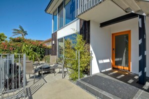 Enter a modern home with a clean design, featuring a glass door and a covered outdoor area with seating.