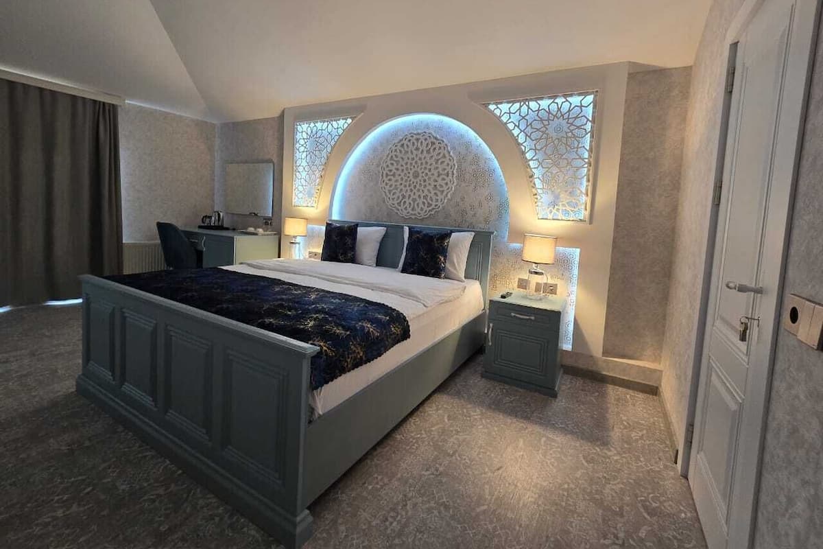 A modern bedroom with a large bed, bedside tables, a decorative wall, and a window with a unique design.