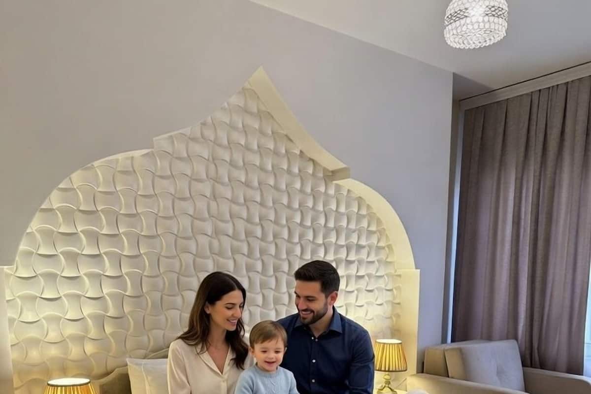 A hotel room with a unique textured headboard, a bed with a swan-shaped pillow, a bedside table with a lamp, and a suitcase on the floor.
