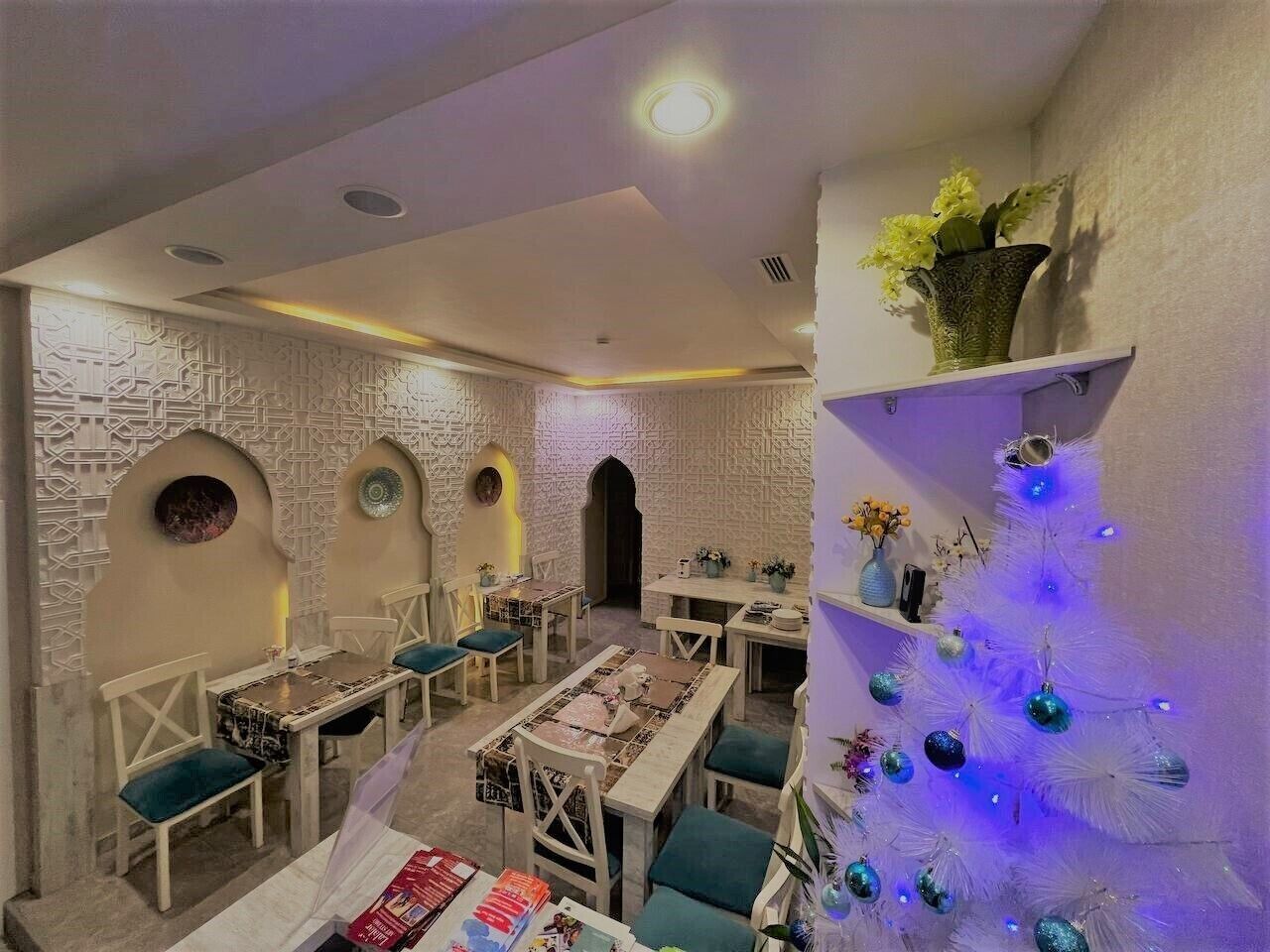 A dining area with tables and chairs, a decorative wall, and a Christmas tree.