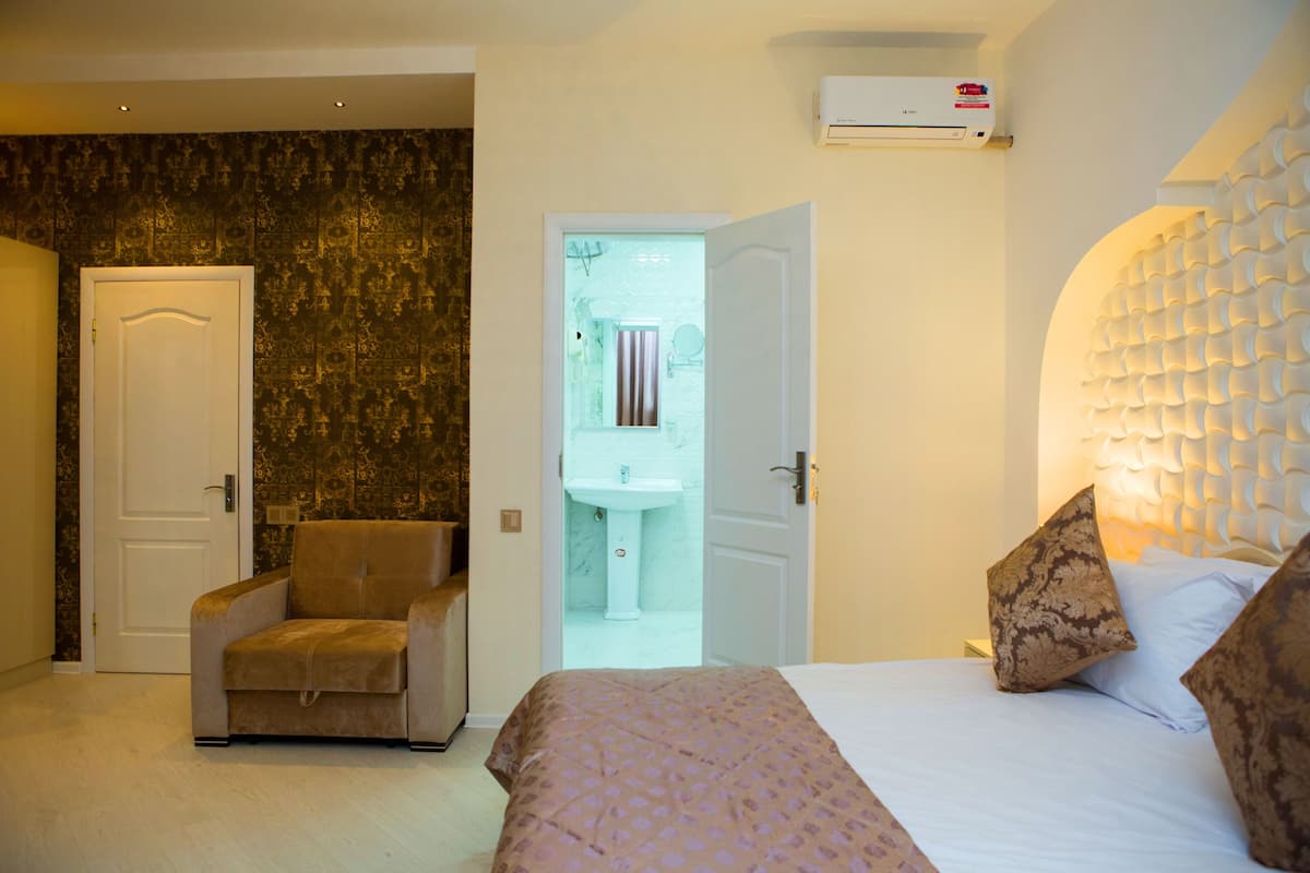 A hotel room with a bed, a chair, a bathroom with a sink, and a door.