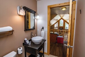 A bathroom with a large white sink, a mirror, and a towel rack. There is a wooden door leading to a balcony with a view of the outdoors.