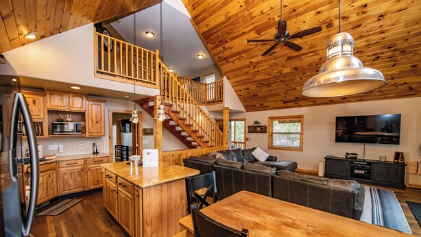 A spacious kitchen with wooden cabinets, a dining area with a wooden table and chairs, a living room with a sofa and a TV, and a staircase leading to an upper level. - Hot Tub! Close to Fishing, ATV, Hiking, Rafting, Rivers! (Pagosa Springs)