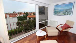 Een balkon met uitzicht op een stadslandschap, een witte tafel, een beige bank en een lijst met een afbeelding aan de muur.