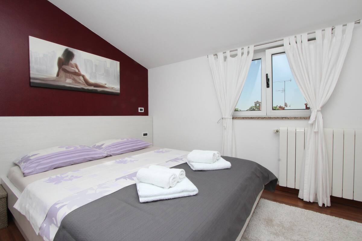 Une chambre à coucher avec un lit, deux serviettes, un tableau et une fenêtre avec des rideaux.