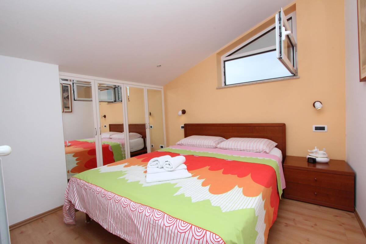 Une chambre à coucher avec un lit, une table de chevet, un miroir et une fenêtre.