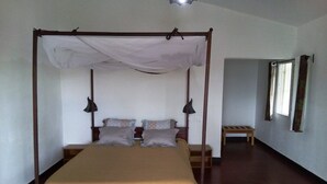 Una cama con dosel, una mesita de noche y un banco en una habitación con suelo de madera y paredes blancas.
