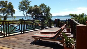 Terraza de madera con dos sillones y plantas en macetas, con vista a un cuerpo de agua y árboles.