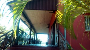 Una escalera conduce a un área techada, con un edificio rojo a la derecha y una palmera a la izquierda.