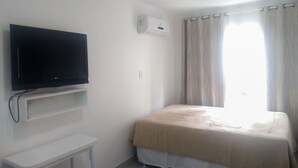 Ein Schlafzimmer mit einem Bett, einem an der Wand befestigten Fernseher, einer Klimaanlage und einem Fenster mit Vorhängen.