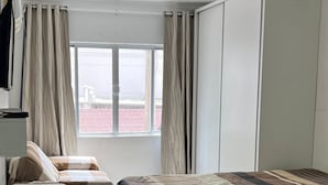 Ein Hotelzimmer mit Bett, Schreibtisch, Stuhl, Kleiderschrank und einem fensterbepflanzten Fenster.