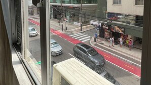 Blick aus einem Fenster eines Gebäudes auf eine Straßenszene, einschließlich einer Fußgängerampel und einer Bushaltestelle.
