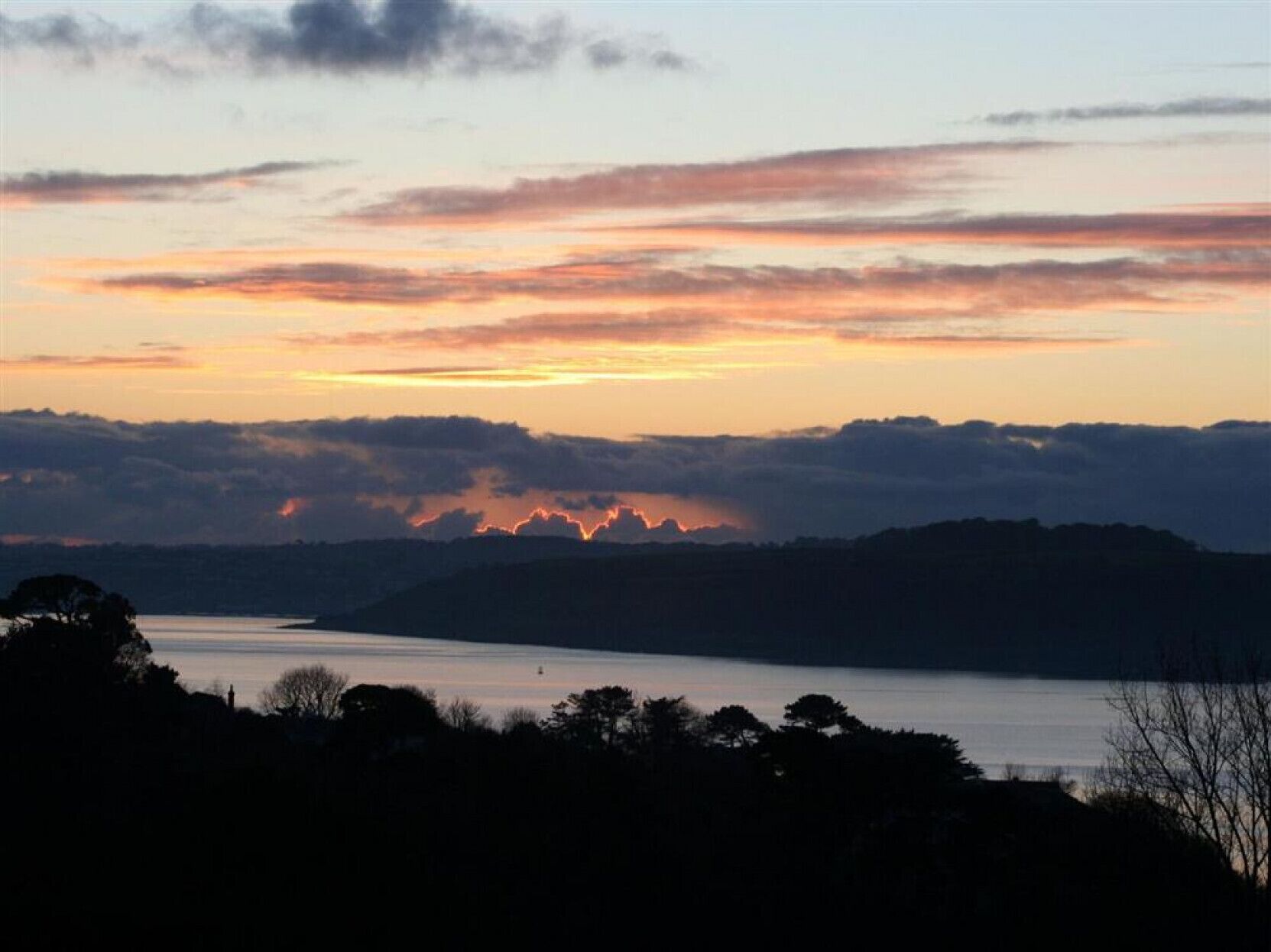 A sunset over a body of water with distant hills.