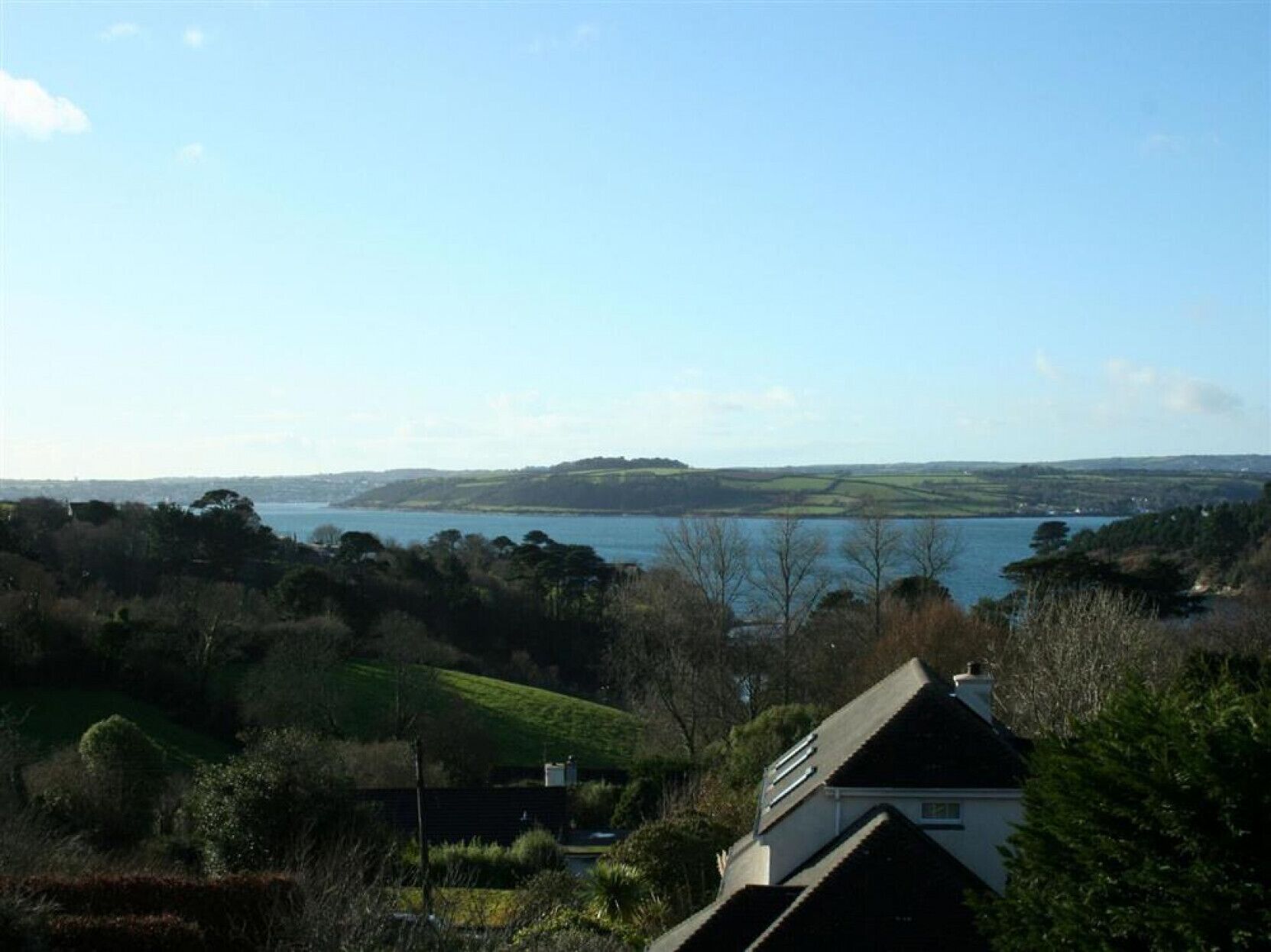 A house with a sloped roof, surrounded by greenery and a view of a lake.