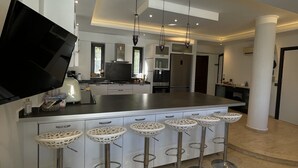 A modern kitchen with a central island, bar stools, and a flat-screen TV. - Esiyok Villa in Antalya with heated pool (Hisarcandir Mahallesi Konyaalti)