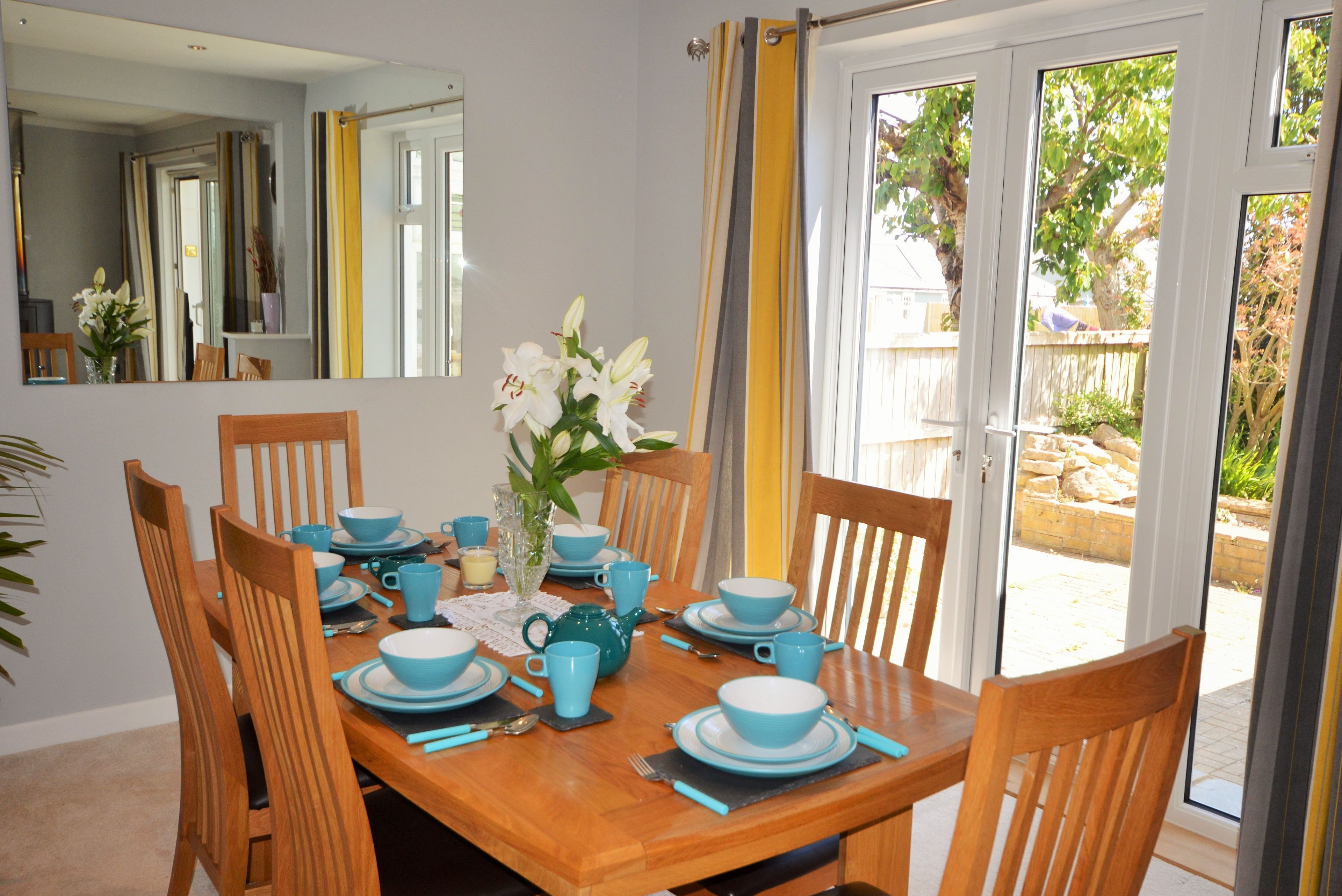 A dining room with a wooden table set for six, blue tableware, and a vase with white flowers.