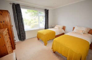 A bedroom with two beds, a wooden dresser, and a window with curtains.