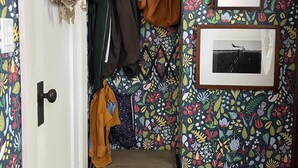 A hallway with a patterned wallpaper, a coat rack with various jackets, a door with a doorknob, and a shelf with shoes. - 1940s Brooklyn Cottage Townhouse (Brooklyn)