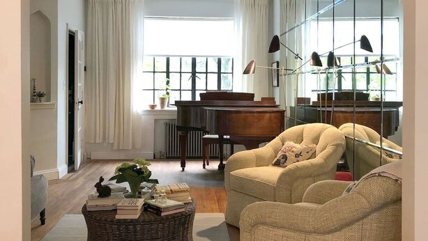 A living room with a piano, a sofa, a wicker coffee table with books, and a large mirror. - 1940s Brooklyn Cottage Townhouse (Brooklyn)