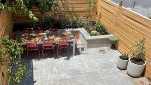 A patio with a table and chairs, surrounded by potted plants and a wooden deck. - 1940s Brooklyn Cottage Townhouse (Brooklyn)
