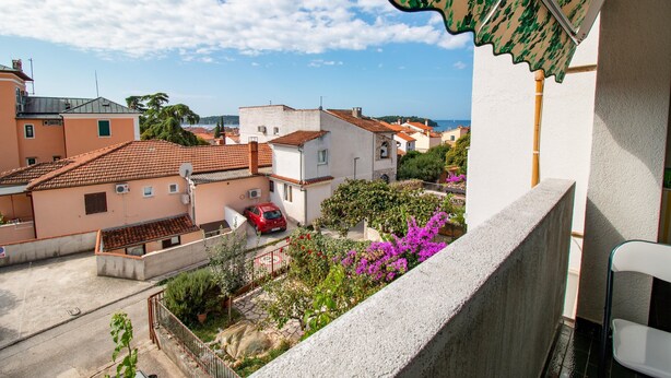Ein Balkon mit Blick auf eine Wohngegend, darunter Häuser und ein rotes Auto, das auf der Straße geparkt ist.