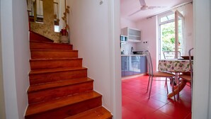 Eine Treppe führt zu einer Küche mit rotem Boden, einem Essbereich mit Tisch und Stühlen sowie einem Deckenventilator.