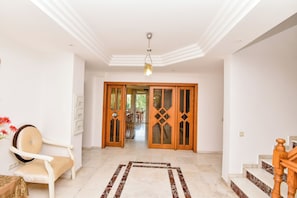 Una habitación amplia con una escalera de madera, una silla blanca y una alfombra estampada.