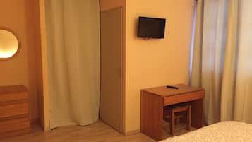 A hotel room with a wooden dresser, a small wooden table, a TV mounted on the wall, and a bed with a floral bedspread.
