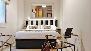 Een slaapkamer met een bed, nachtkastje, spiegel en raam.