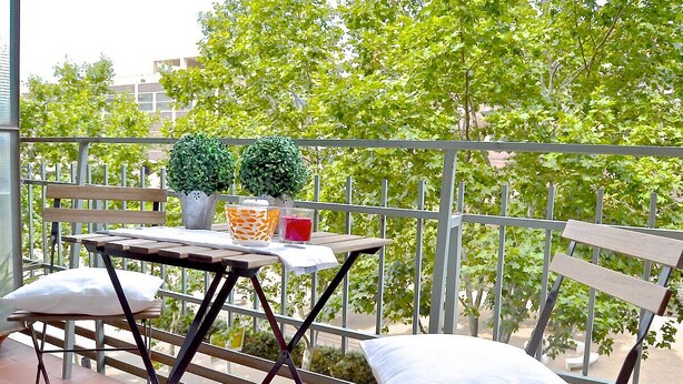 Een balkon met een tafel, twee stoelen en een potplant.