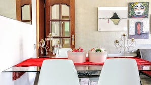Een eethoek met een glazen tafel, witte stoelen, een rode tafelkleed en decoratieve objecten, waaronder twee roze vazen met bloemen.