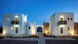 Un bâtiment moderne aux murs blancs, doté d’une façade en pierre, d’une arche centrale et de deux balcons avec des garde-corps.