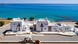Un bâtiment situé sur la côte, avec des murs blancs et des fondations en pierre, qui offre une vue sur une mer d’un bleu limpide.