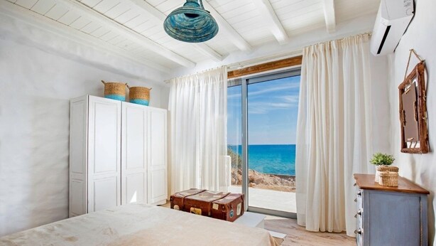 Une chambre à coucher avec un lit, une armoire, une commode, une valise et une vue sur la mer.