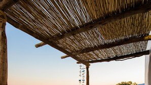 Une terrasse avec une table et des chaises blanches, donnant sur une plage et la mer.