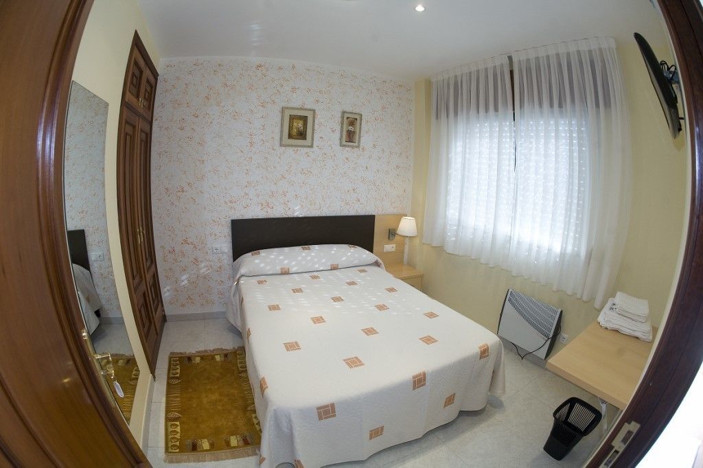 A hotel room with a bed, a desk, a chair, a radiator, and a window with curtains.