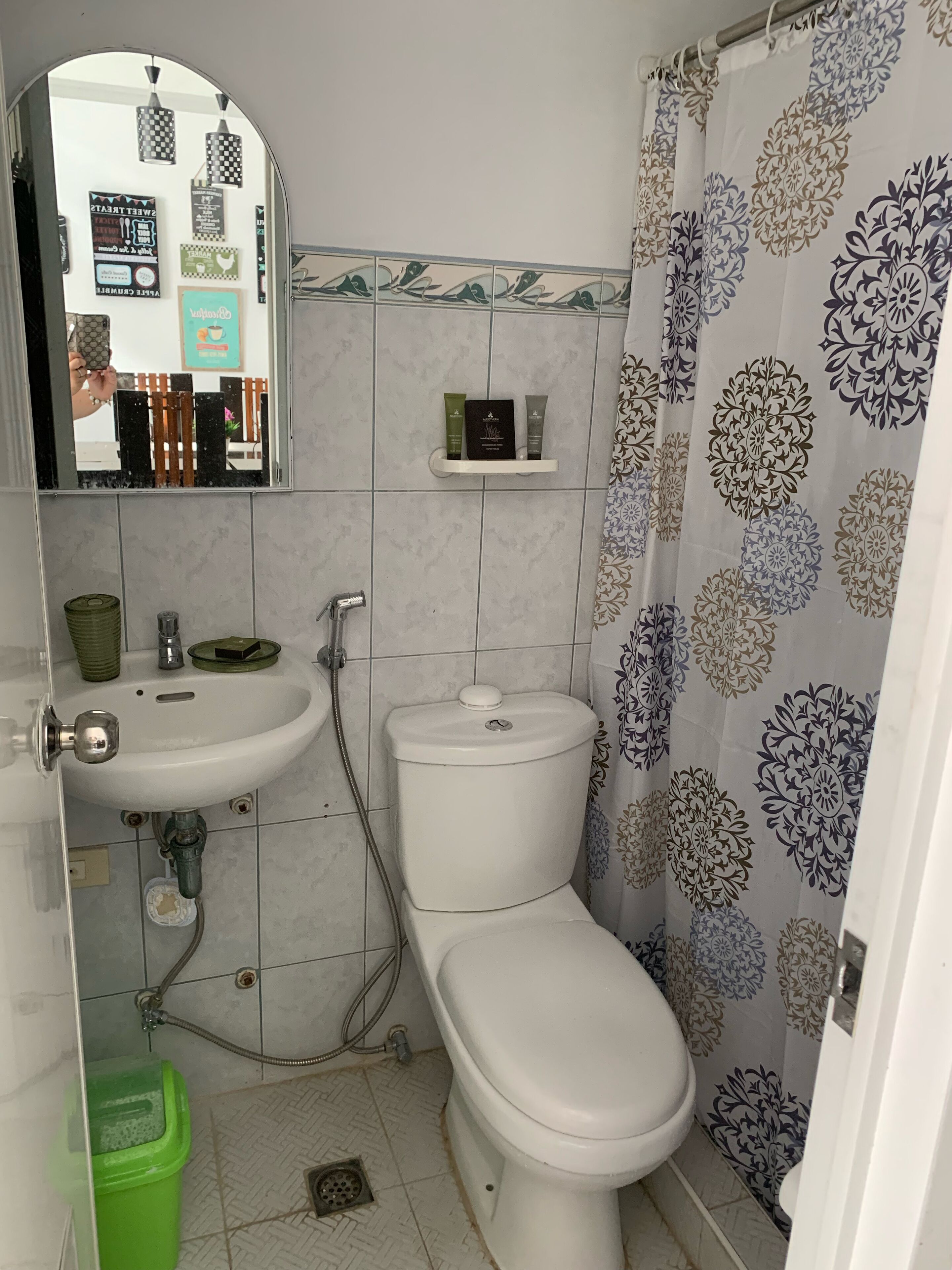 Un bagno con WC, lavabo e doccia. Si nota uno scaffale con articoli da toilette e uno specchio sopra il lavabo.