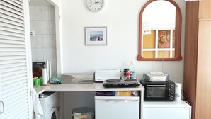 A compact kitchen with a washing machine, a small refrigerator, a microwave, and a sink.