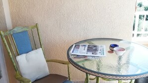 A chair with a cushion and a glass table with a newspaper and a candle.