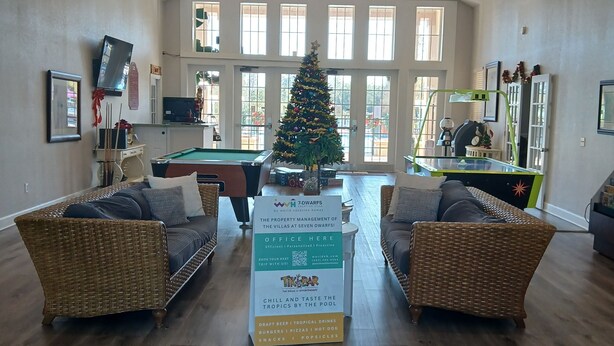 Eine geräumige Lobby mit Billardtisch, zwei Korbsesseln, einem Weihnachtsbaum und einem Schild für die Hausverwaltung '7-Dwarfs'.