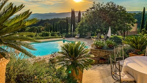A pool area with lounge chairs and a table, surrounded by greenery and a view of the sunset. - Country House Villa Rey (Panicale)
