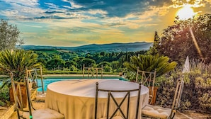 A round table with a white tablecloth and four chairs, surrounded by lush greenery and a pool. - Country House Villa Rey (Panicale)