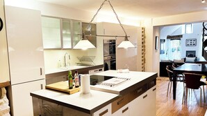 A modern kitchen with a central island, stainless steel appliances, and a dining area with a wooden table and chairs. - Forcalquier Architecture Village House Center (Forcalquier)