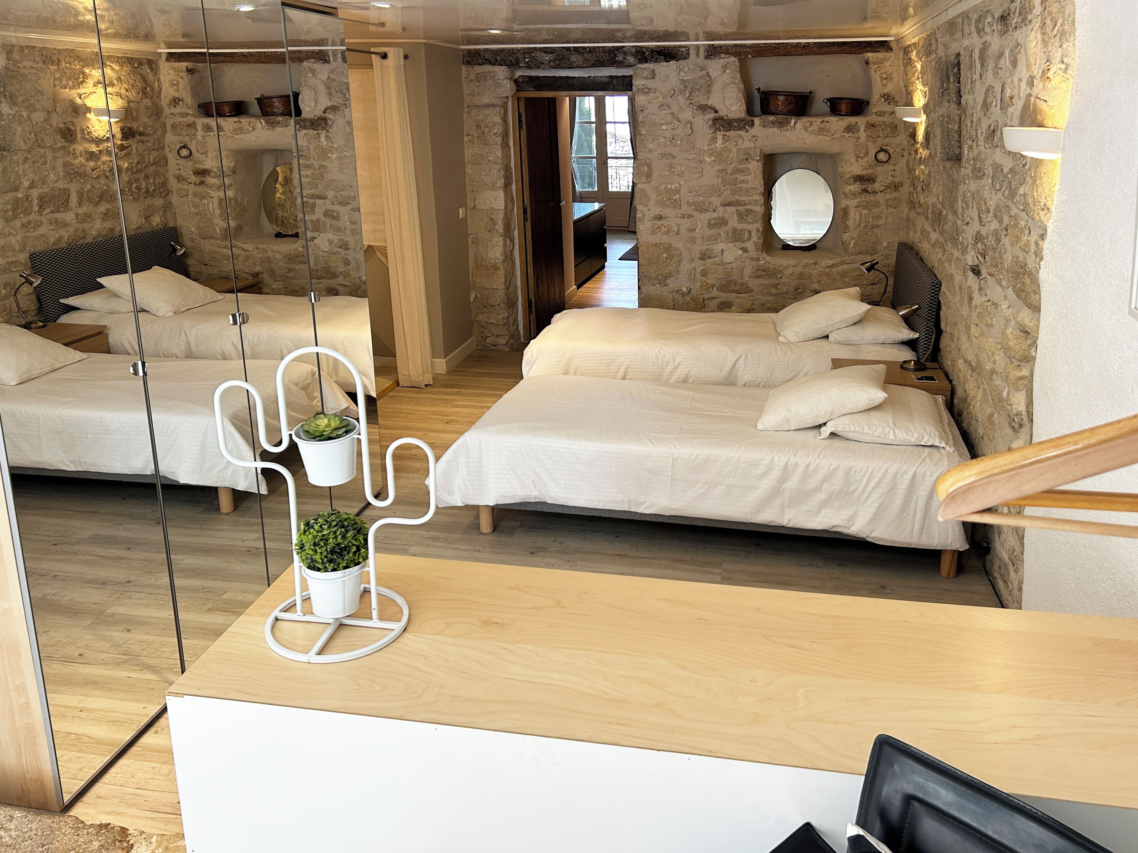 A hotel room with two beds, a wooden desk, and stone walls.