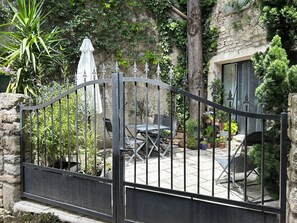 A gated patio area with a table and chairs, surrounded by potted plants and a stone wall. - Forcalquier Architecture Village House Center (Forcalquier)