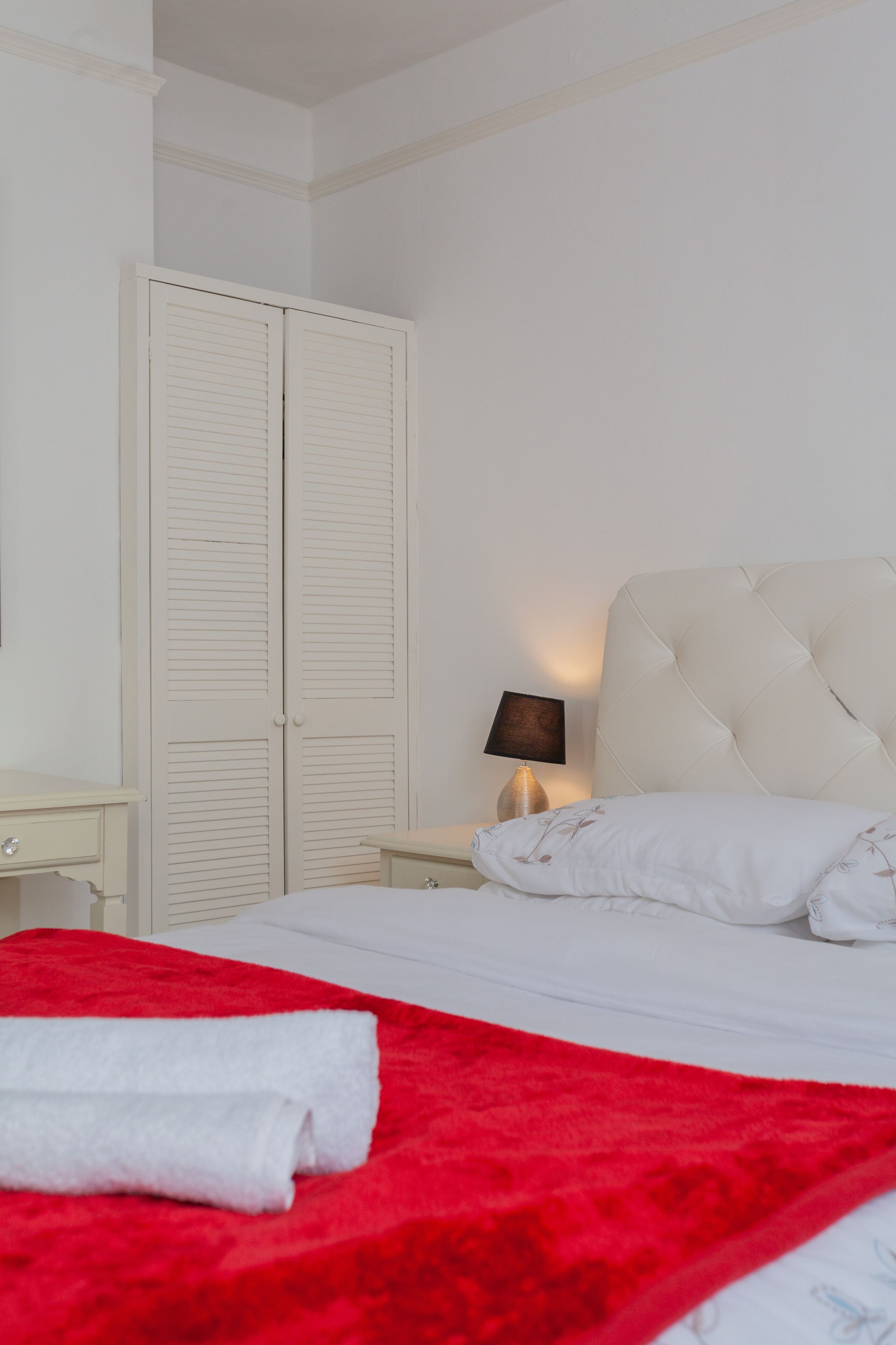 A bedroom with a bed, a nightstand, a lamp, and a wardrobe.