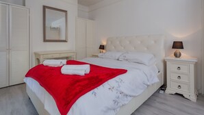 A bedroom with a large bed, white walls, a mirror, a bedside table with a lamp, and a wardrobe. - Windsor House - A Home from home (Derry)